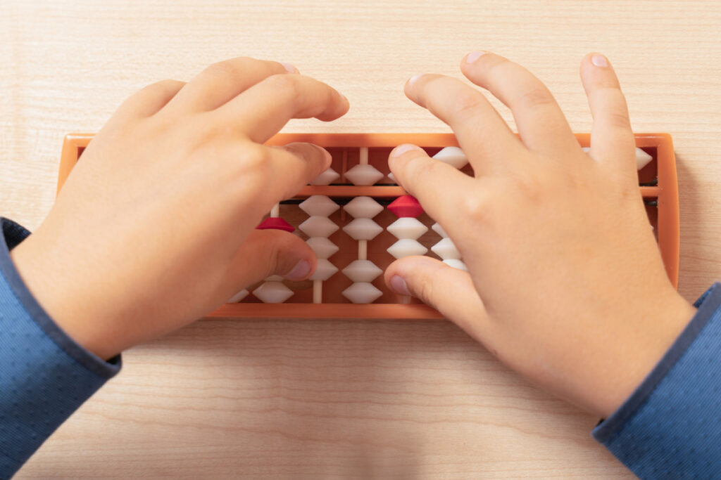 Foto das mãos de uma criança mexendo em um soroban