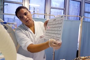 Terapeuta Ocupacional intermediando a comunicação de um paciente internado na UTI com prancha de comunicação do alfabeto e ponteira a laser para cabeça