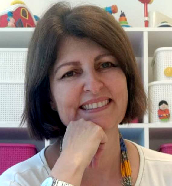 Foto de Miryam Pelosi sorrindo, com uma mão apoiada no queixo.