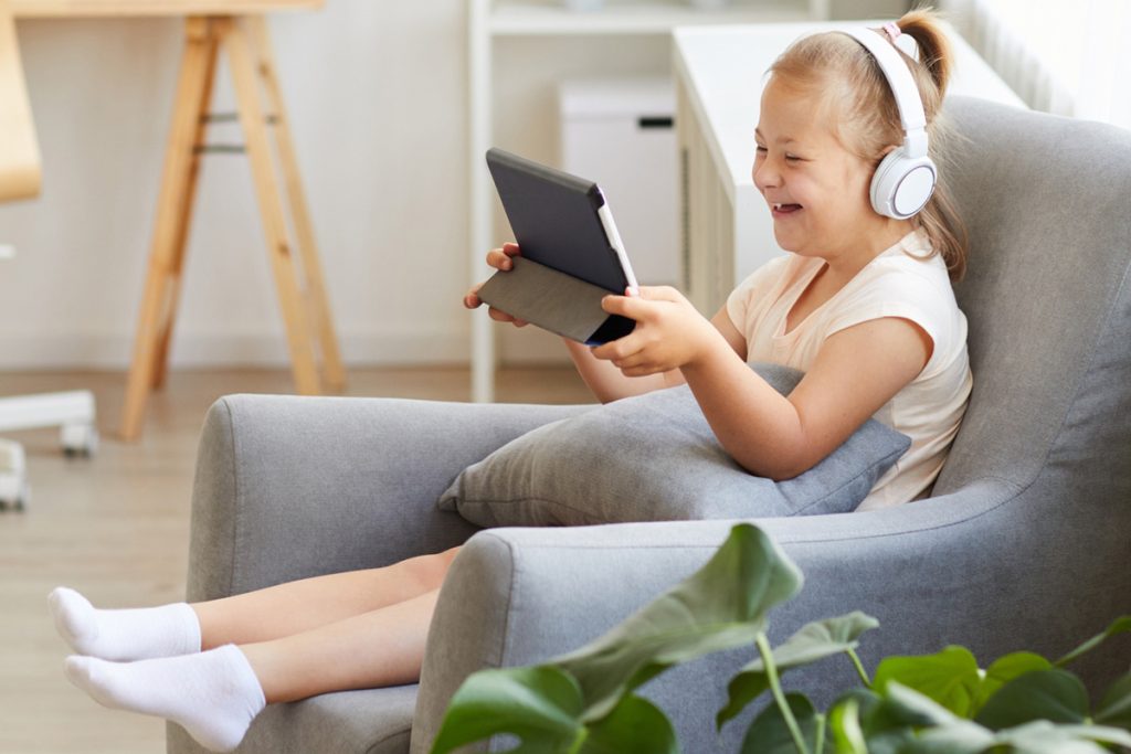 Criança sentada no sofá, com um fone de ouvido, vendo livro acessivel em um tablet