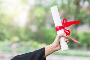 Uma mão feminina levanta ao alto um diploma enrolado em uma fita vermelha