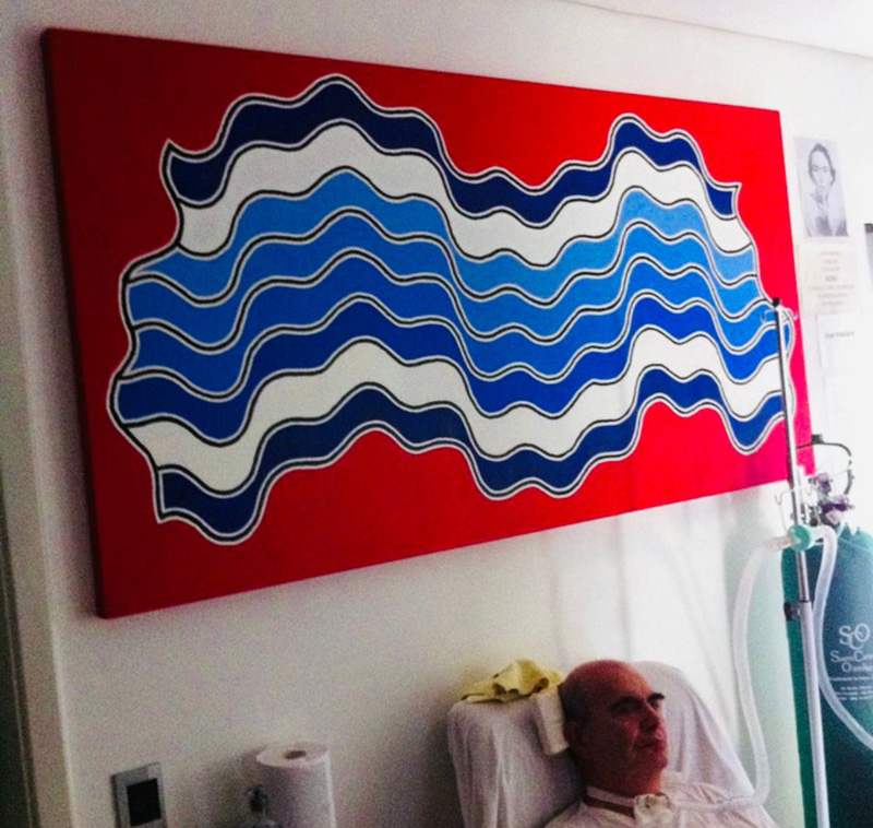 Foto de uma tela vermelha com grafismos em tons de azul e abaixo da tela um senhor traqueostomizado sentado em uma poltrona