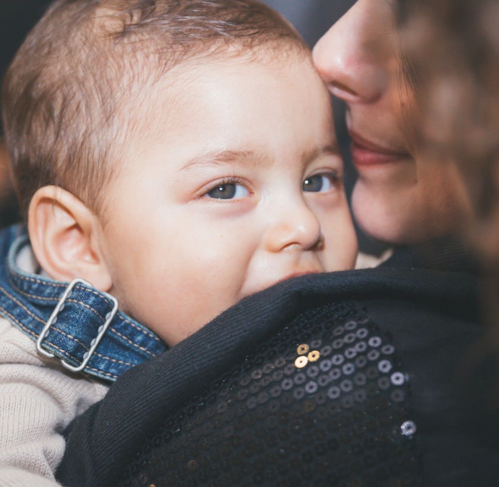 Foto em close de um bebê de olhos e cabelos claros no colo de sua mãe.