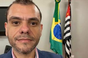 Foto do Thiago em close, com as bandeiras do Brasil e de São Paulo ao fundo.