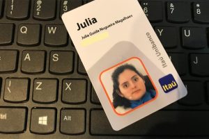 Foto de um teclado preto de computador e sobre ele um crachá de funcionário do banco Itaú Unibanco com o nome e foto da Julia.