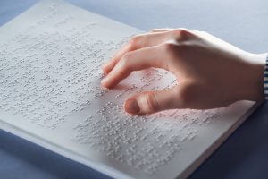 Foto em close de uma mão jovem passando os dedos sobre uma placa branca com texto em Braille