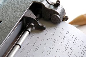 Foto em close de uma máquina braille, mostrando um papel impresso em braille