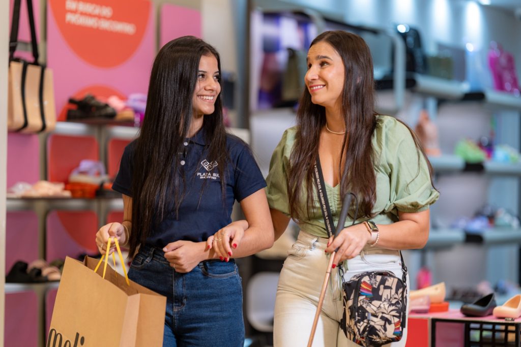 Foto da influencer Geisa Farini junto com uma funcionária do Shopping Plaza Sul andando dentro de uma loja de sapatos com uma sacola na mão.