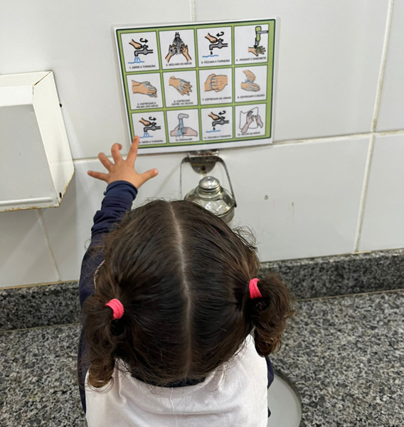 Garotinha no banheiro olhando uma prancha de CAA de rotina para lavar as mãos