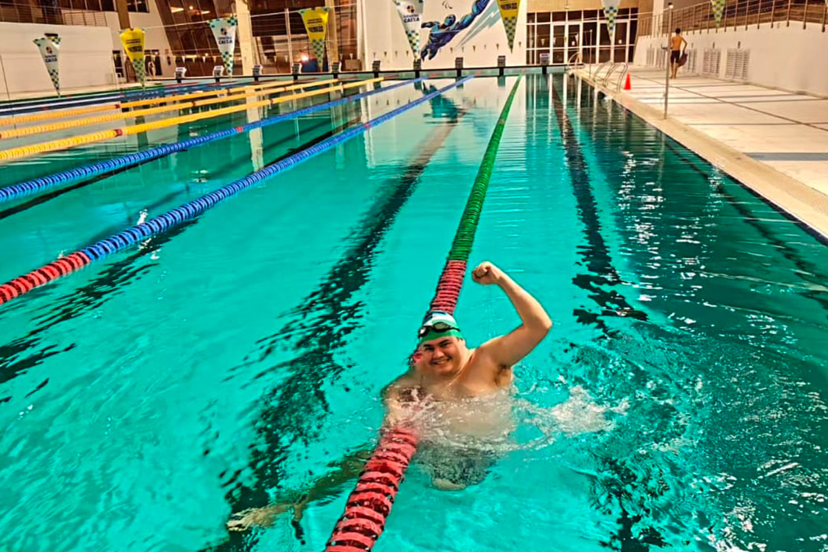 Foto de Ezequiel na piscina do Centro Paralímpico fazendo sinal de vencedor com o braço.