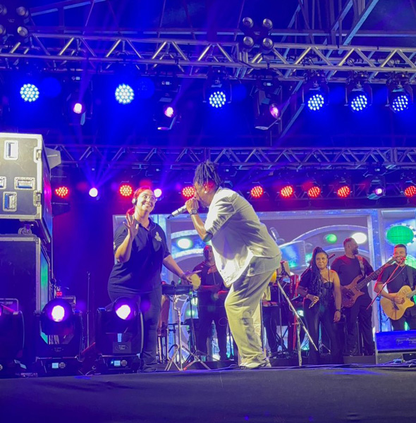 Foto de Fernanda em cima de um palco durante um show traduzindo a música em Libras. O cantor está interagindo com ela.