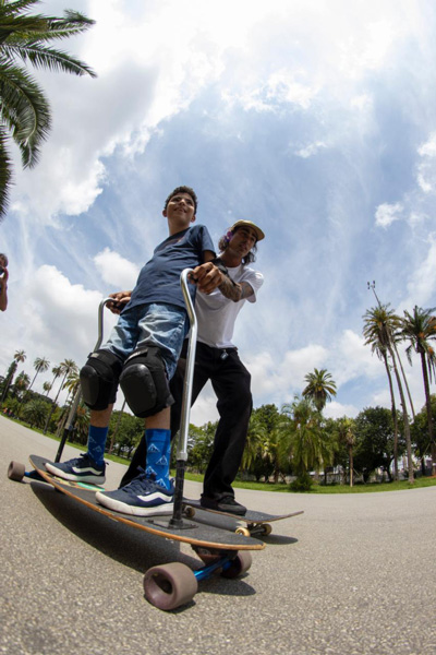 Foto de um garoto se divertindo andando de skate adaptado com a ajuda de outro skatista