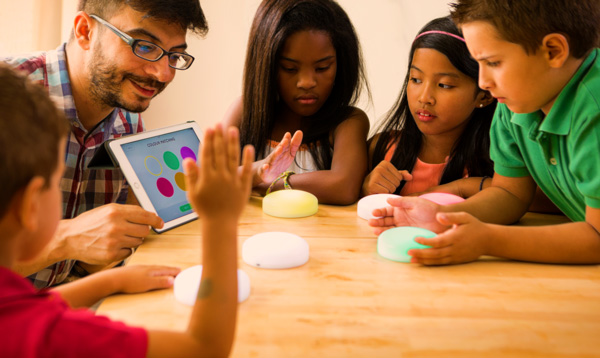 Foto de um professor segurando um tablet e alguns alunos ao seu redor com acionadores coloridos
