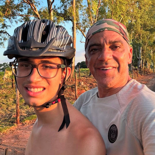 Foto de Mateus suado com capacete e sem camisa ao lado do seu pai Geraldo em uma trilha