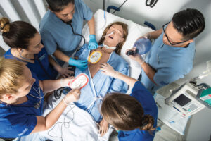 Foto de diversos alunos da área de saúde treinando procedimentos de emergencia com um simulador de paciente em um ambiente hospitalar