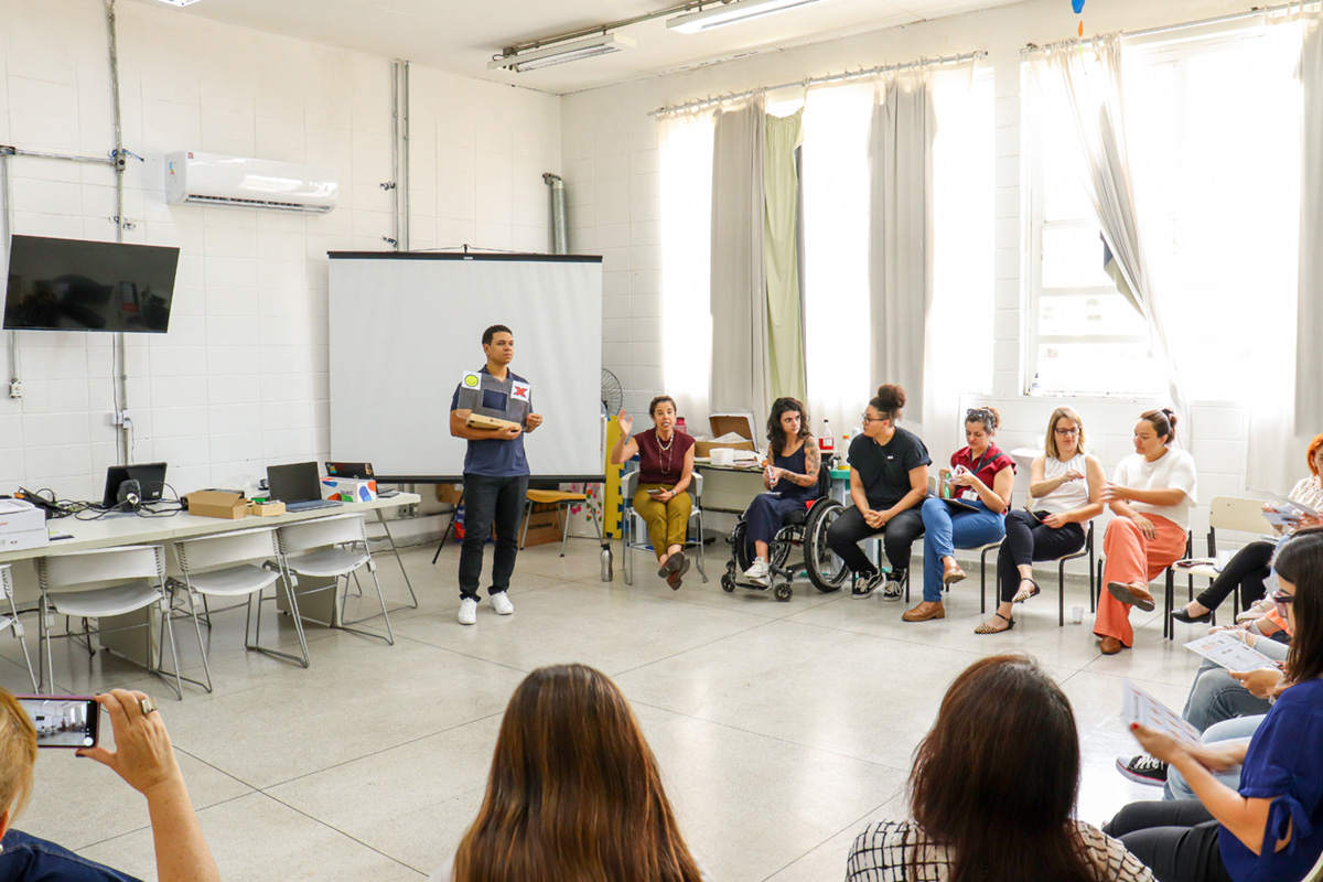 Foto de um rapaz apresentando um recurso de tecnologia assistiva para uma plateia em Taubaté