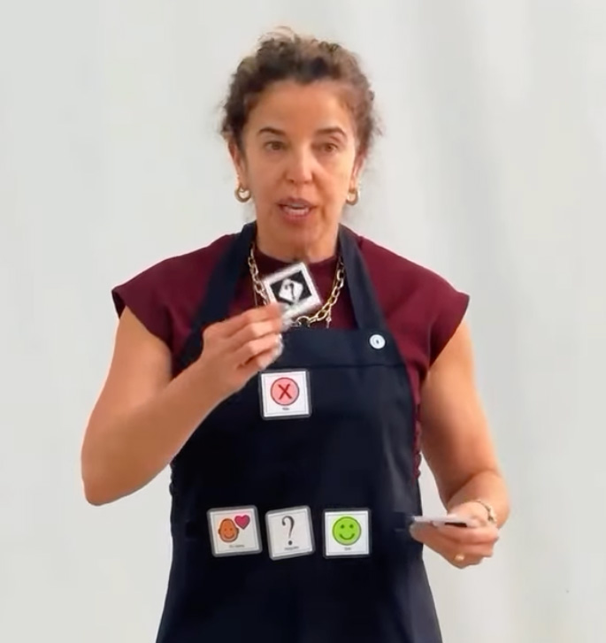 Foto de Silvia vestindo um avental de comunicação alternativa com diversos pictogramas