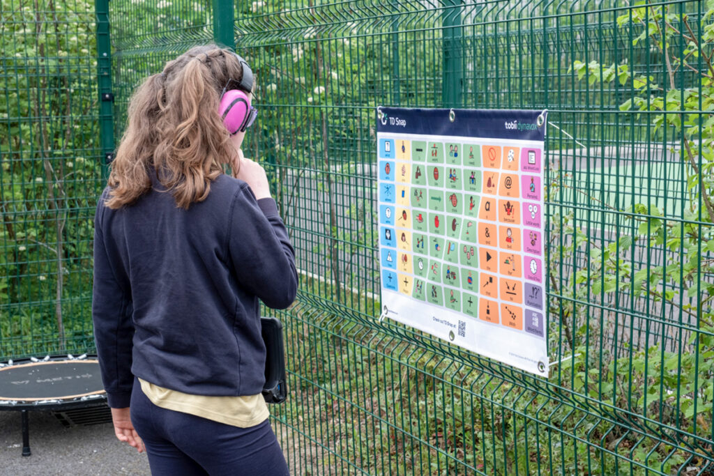 Foto de uma garota usando abafador nos ouvidos olhando um poster de CAA em um parque.