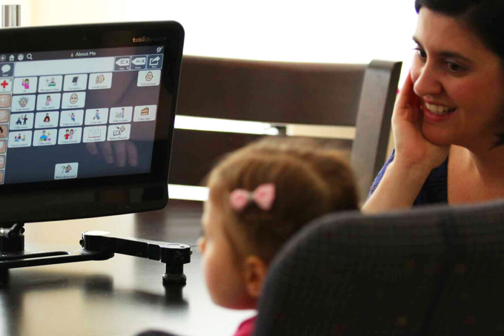 Foto de uma garotinha se comunicando com sua mãe através de um recurso de tecnologia assistiva -  tablet de Comunicação alternativa com controle pelo olhar