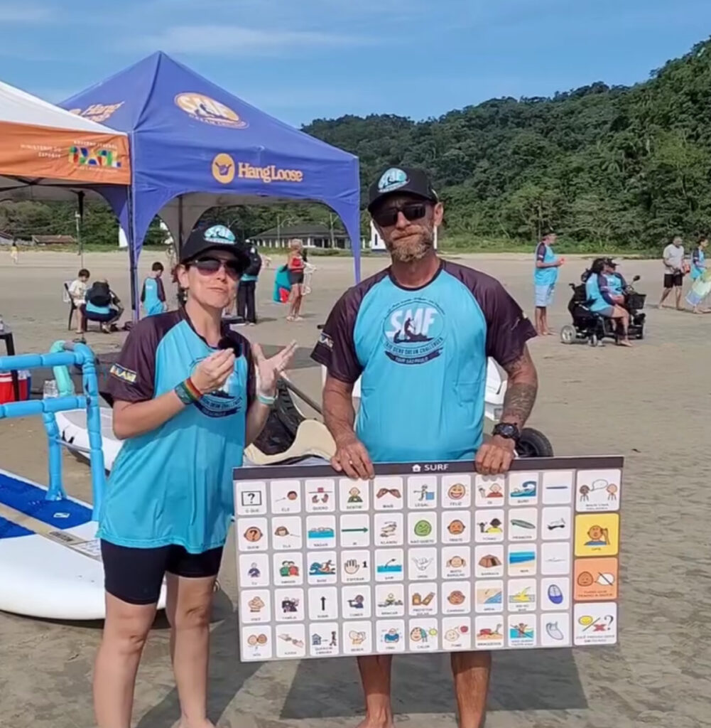 Foto de Dafne e Cebola na praia segurando uma prancha de Comunicação Alternativa grande