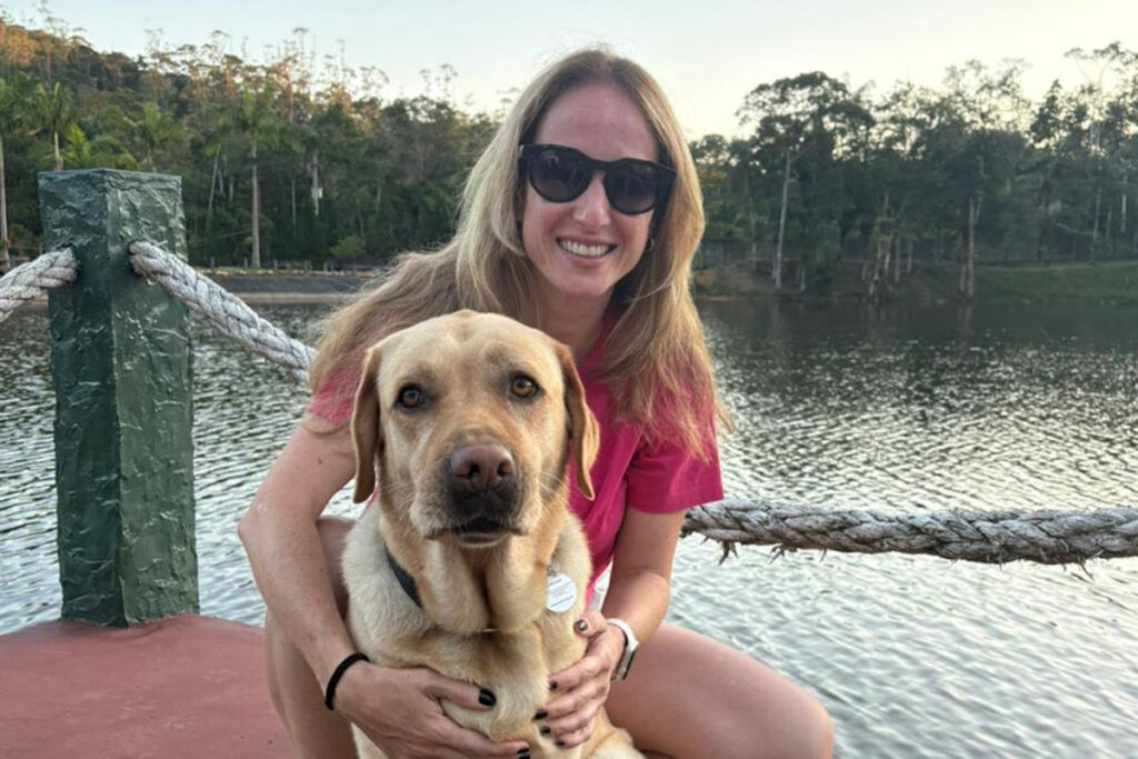 Foto de Juliana abraçada ao labrador Quindim em frente a um bonito lado
