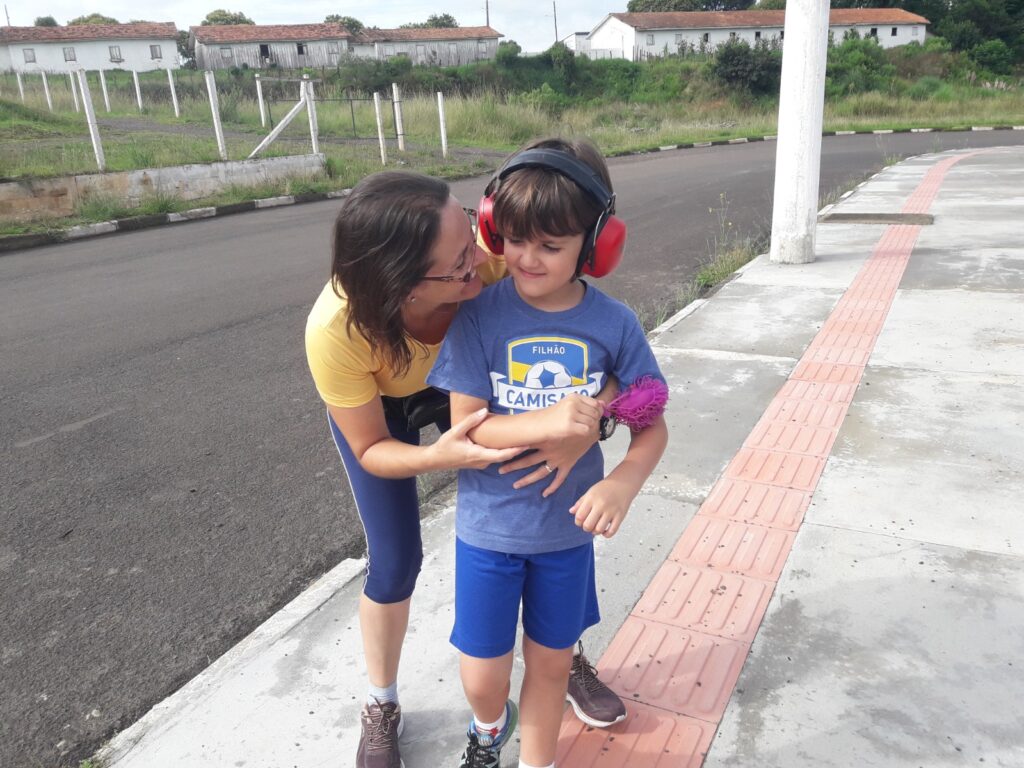 Foto de Giselle abraçando seu filho Pedro, que está usando abafadores.