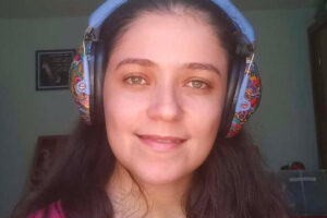 Foto de Carol sorrindo dentro de casa usando um abafador de ruídos