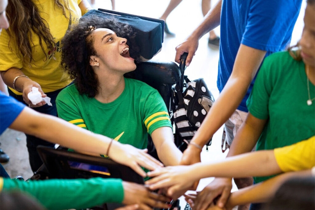 Foto de uma menina cadeirante usando tecnologia assistiva com comunicação alternativa para torcer na Copa do Mundo com os amigos
