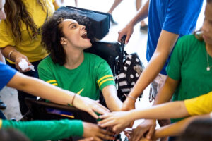 Foto de uma menina cadeirante usando tecnologia assistiva com comunicação alternativa para torcer na Copa do Mundo com os amigos