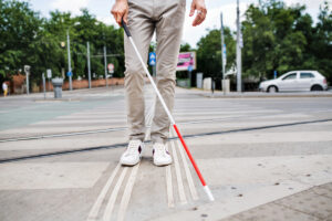 Pessoa caminhando com uma bengala branca e vermelha, utilizada por pessoas com surdocegueira para orientação e mobilidade.