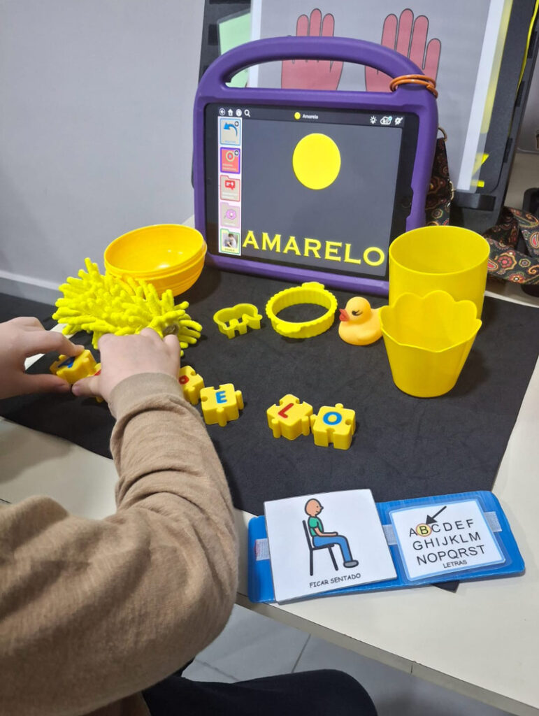 Foto de uma criança com uma atividade sobre a cor amarela. Ela está com um tablet com o TD Snap com a cor amarela, e diversos objetos amarelos em sua frente.