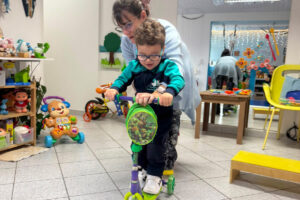 Foto de Dafne brincando com uma criança com um patinete em uma sala cheia de brinquedos