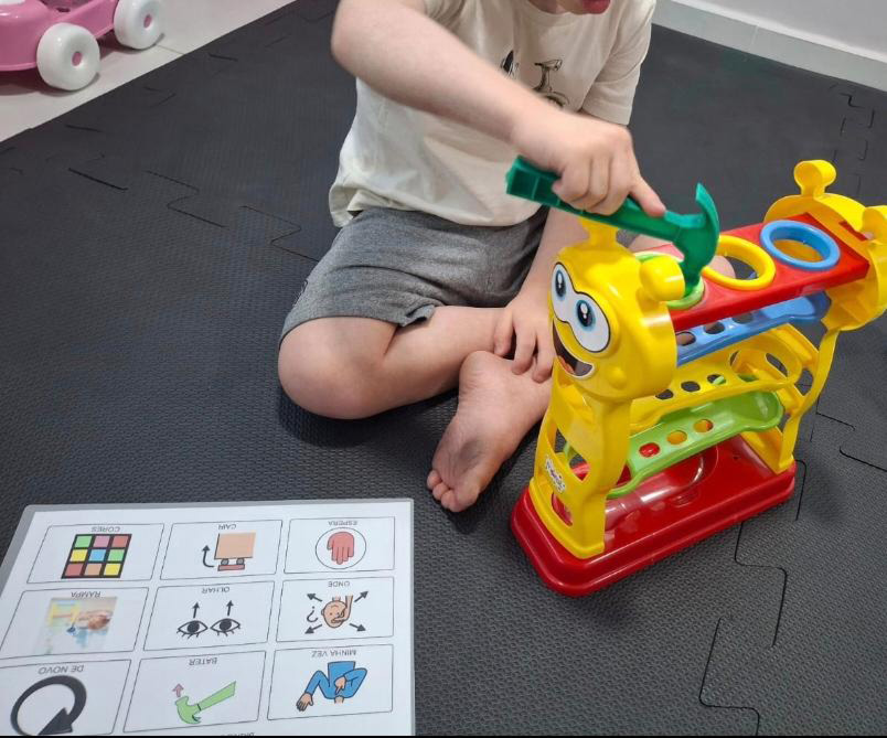 Foto de um garoto brincando com um brinquedo colorido e usando um livro de CAA.