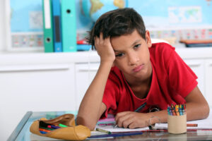 Garoto com TDAH entediado numa mesa escolar.