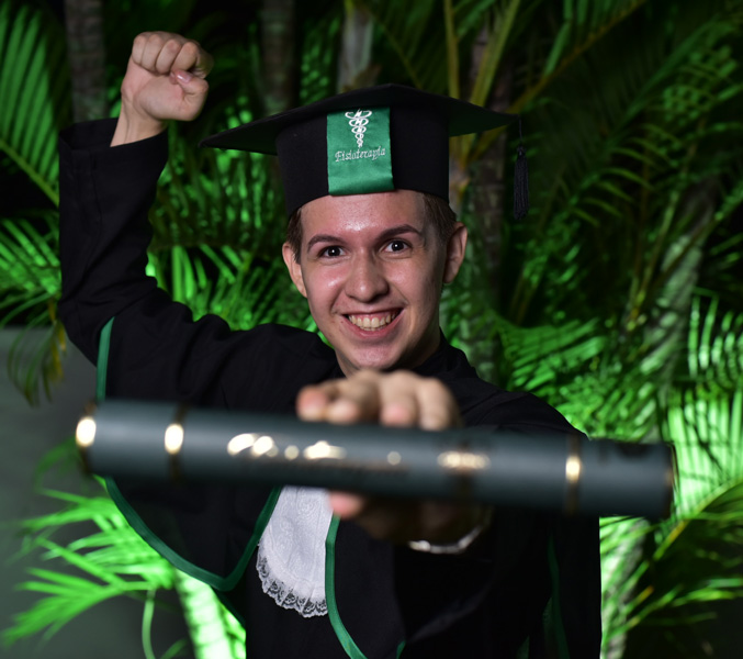 Foto de Ítalo vestindo beca mostrando o seu diploma de fisioterapeuta.