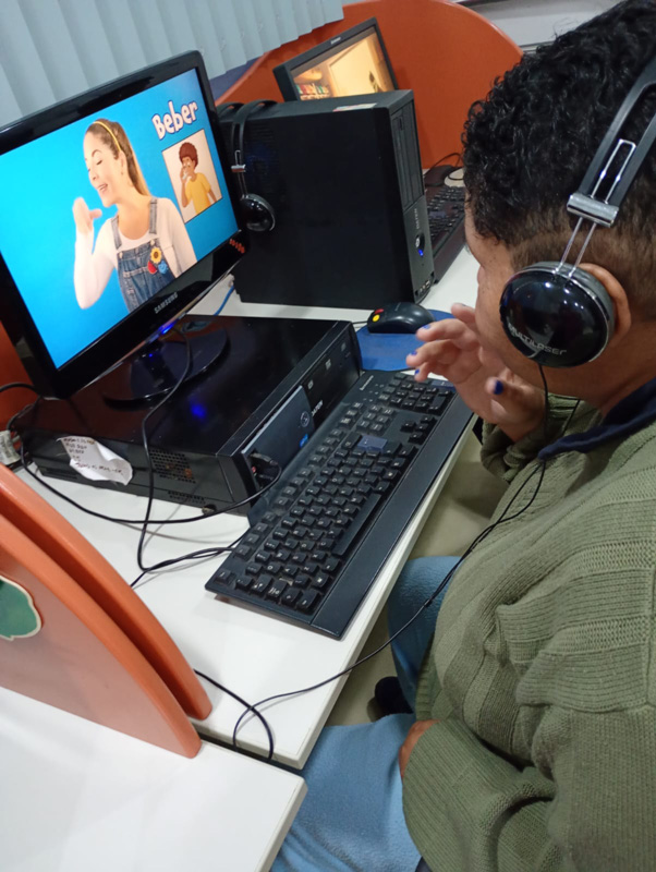 Pessoa utilizando um computador com fones de ouvido durante uma atividade de comunicação e aprendizado.