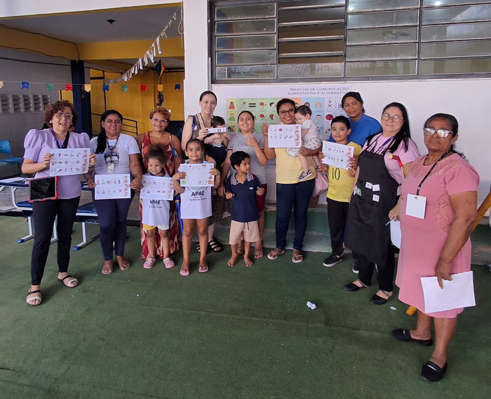 Foto de Adriana em uma escola com alguns professores segurando pranchas de CAA após um curso.