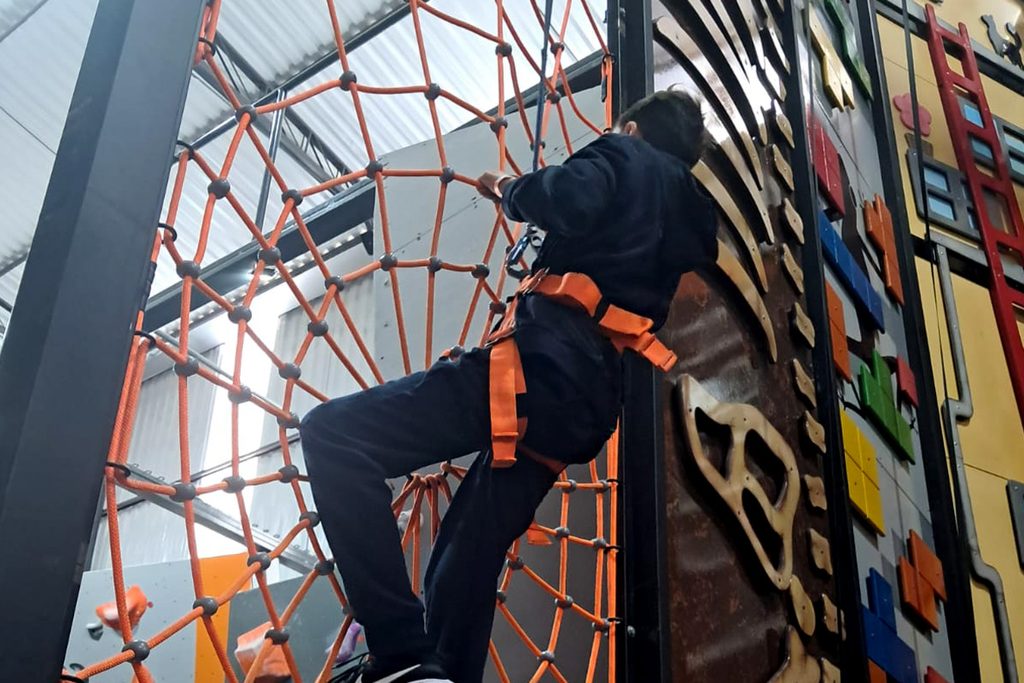 Foto de um menino fazendo uma escalada em uma teia de um parque indoor