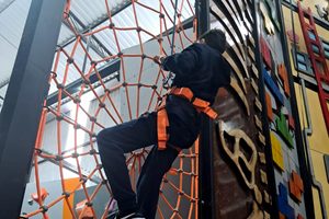 Foto de um menino fazendo uma escalada em uma teia de um parque indoor