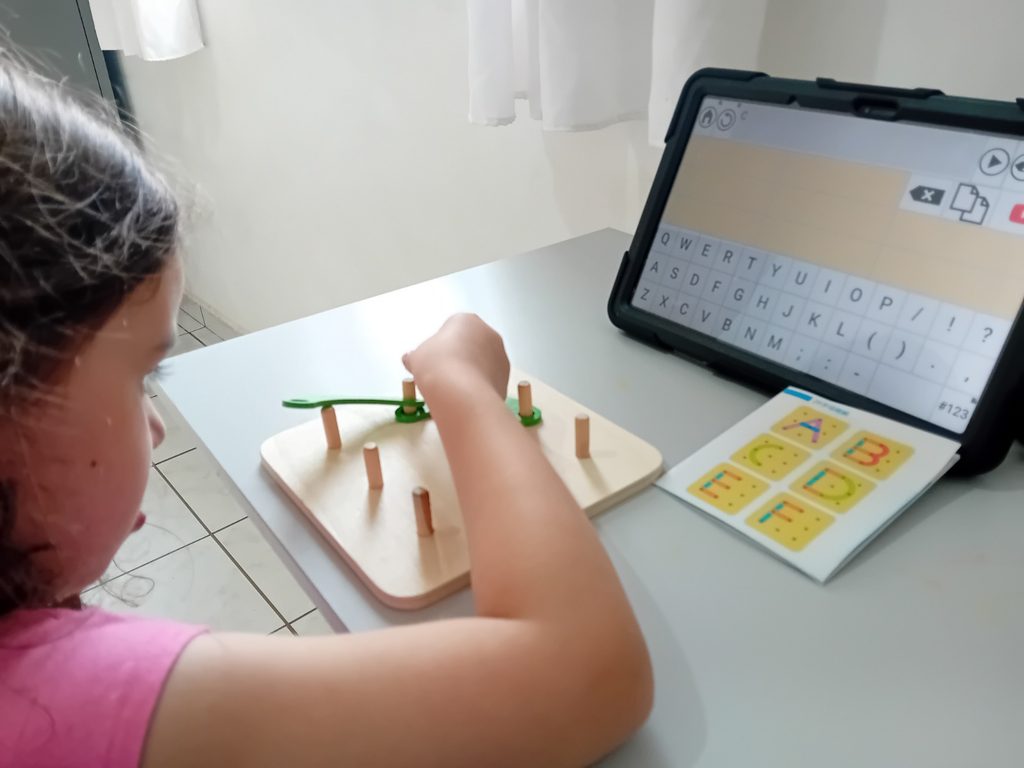 Foto de Adelina usando seu tablet de CAA junto com construções de letras.